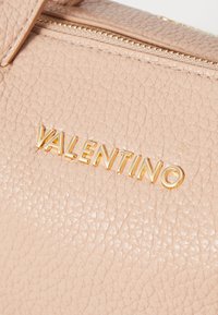 Bolsa de mão em pele rosa clara, com uma superfície texturizada e o logótipo "VALENTINO" em tom dourado. Detalhe de zipper na parte superior adiciona funcionalidade.