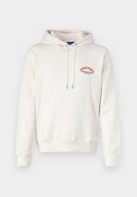Haut à capuche de couleur crème en tissu doux, doté d'une poche kangourou et d'un logo graphique rouge sur la poitrine. Cordon de serrage avec embouts en métal.