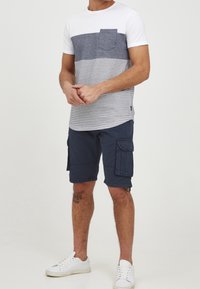 Pánské tričko s krátkým rukávem s bílým a námořnicky modrým pruhovaným vzorem a kapsou na hrudi, doplněné o námořnicky modré cargo kraťasy a bílé tenisky.