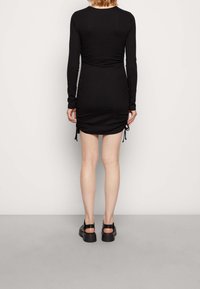 Svart långärmad klänning med samlade detaljer på sidorna, försedd med dragsko. Släta tyger, åtsittande silhuett, längd till mitten av låret.