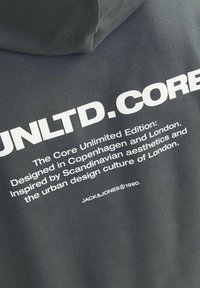 Donkergrijze hoodie met bold witte tekst. Bevat "UNLTD.CORE" en details over het ontwerp geïnspireerd door Kopenhagen en Londen. Zachte stof.