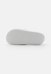 Semelle de sneaker blanche avec un motif de grille texturé, présentant une empreinte de logo et une finition lisse et solide, offrant traction et durabilité.