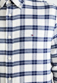 Gestricktes Flanellhemd in Weiß mit Marine- und Blautönen. Verfügt über einen Button-Down-Kragen und ein dezentes Logodetail auf der Brust. Weiche Textur.