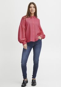 Rotes, kurzärmliges Hemd mit Wabenmuster, schulterfreien Ärmeln und Kragen, kombiniert mit dunkelblauen Skinny Jeans und schwarzen Schuhen.