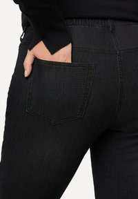 Jeans de mezclilla negros con un diseño ajustado, que cuentan con un bolsillo trasero estándar y una cintura elástica para mayor comodidad. Textura suave con detalles de costura mínimos.