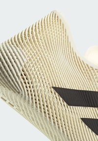 Κοντινό πλάνο σε μπεζ σόλα παπουτσιού τρισδιάστατης εκτύπωσης με υφή και δομή πλέγματος, και δύο μαύρες γωνιακές ρίγες στο πλάι.