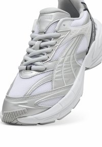 Baskets de course blanches et argentées en matériaux en mesh et synthétiques, avec une semelle texturée, des lacets de couleur assortie et un logo bien visible.