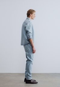 Φωτεινό γαλάζιο τζιν μπουφάν και τζιν παντελόνι σε ταιριαστό χρώμα, συνδυασμένα με σκούρα καφέ μπότες. Το ντύσιμο έχει άνετη εφαρμογή και εμφανείς ραφές.