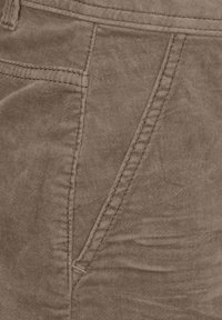 Pantalons en coton marron avec une texture douce, présentant des coutures évidentes le long des poches latérales et une finition lisse légèrement froissée.