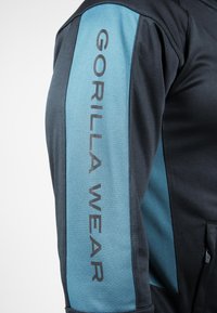 Zwarte sweatshirt met lichtblauwe zijpaneel waarop "GORILLA WEAR" in vetgedrukte, donkere letters staat. De stof lijkt glad met atletische ontwerpelementen.