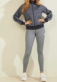 Giacca zip-up navy in tessuto fantasia, abbinata a leggings bianchi e navy con motivo. Sneakers bianche completano l'outfit.