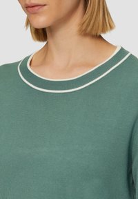 Sweter z mieszanki bawełny w stonowanej zieleni z białym prążkowanym okrągłym dekoltem. Tekstura jest gładka, a fason jest dopasowany.