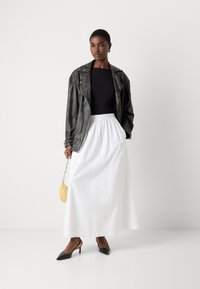 Veste en cuir noir, haut noir ajusté, jupe blanche fluide et escarpins à lanières. Les accessoires comprennent un petit sac à main jaune.