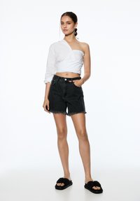 Vit långärmad skjorta med en axel blottad, tillsammans med svarta denimshorts med fransade kanter och en standard midjeband. Svarta sandaler med sula.