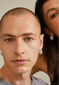 Pendientes de aro plateados con una superficie texturizada, que presentan un diseño brillante. Primer plano de una persona que lleva pendientes, vestida con un suéter gris.