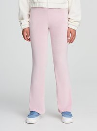 Różowe, prążkowane spodnie rozszerzane wykonane z miękkiej tkaniny, o fakturowanej powierzchni. Połączone z niebieskimi sneakersami i lekką kurtką.