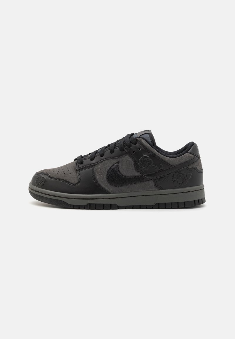 Baskets basses noires et gris foncé avec des panneaux en cuir et en daim, logo Nike, embossage floral et lacets noirs sur une semelle plate.