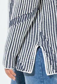 Maglione lavorato a maglia con strisce blu navy e bianche, caratterizzato da una spacco laterale e un tessuto testurizzato. Da abbinare a jeans di denim.
