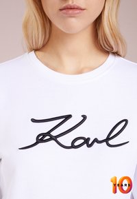 T-shirt bianco in cotone con testo ricamato nero che dice "Karl" sul petto, scollatura rotonda e maniche corte.