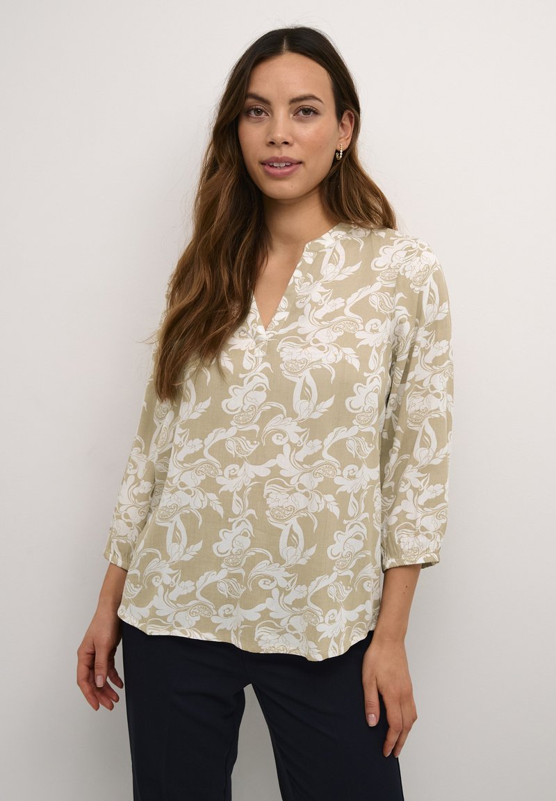 Blusa beige chiaro con motivo floreale bianco, scollatura a V e maniche tre quarti. Realizzata in un tessuto testurizzato. Design semplice e morbido.