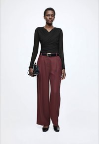 Svart långärmad omlottopp kombinerad med vinröda, vida byxor med hög midja, fastsatta med ett svart bälte, och avslutade med svarta skor.