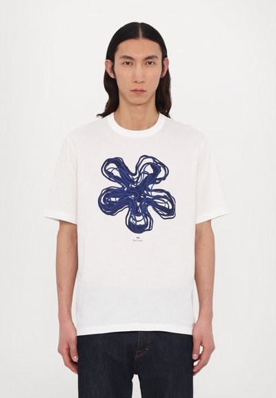 Tricou alb din bumbac, cu un design abstract de floare albastră în centru. Mâneci scurte și decolteu rotund. Blugi din denim închis.