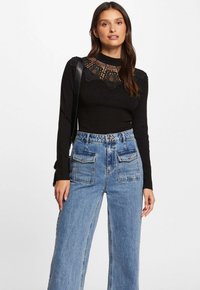 Top negro de manga larga con detalles de encaje en el escote, combinado con jeans de mezclilla azul de pierna ancha que cuentan con grandes bolsillos con parche.