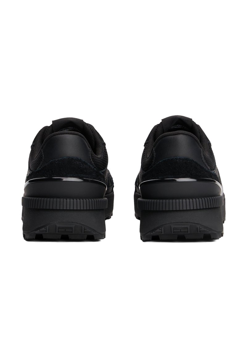 Zapatos deportivos negros con una parte superior texturizada que combina malla y ante, suela gruesa de goma y detalles de diseño minimalistas.