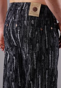 Schwarze und graue Denim-Jeans mit gestreiftem Muster, ausgestattet mit kupferfarbenen Nieten, Gesäßtaschen und einem gebrandeten Lederpatch am Bund.