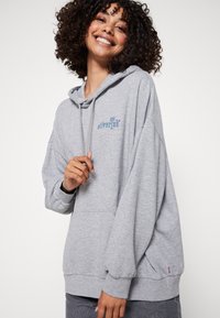 Sudadera holgada gris hecha de una mezcla de algodón. Cuenta con capucha con cordón, puños acanalados y un pequeño logo azul en el pecho.