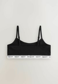 Mustahko musta bralette yläosa säädettävillä olkaimilla, jossa on valkoinen jousto-nauha, jossa lukee "NEXT" mustalla tekstillä alareunassa. Sileä kangas.