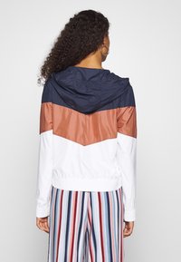 Color-blocked jacket featuring navy, terracotta, and white panels, a hood, and elastic cuffs. Striped pants add a contrasting pattern.