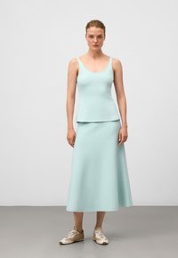 En figursydd, ljus mintgrön klänning med peplum-midja, som har tunna axelband och en mjuk textur, i kombination med beige sneakers.