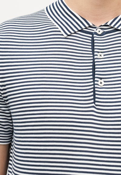 Polo à rayures horizontales bleu marine et blanches avec trois boutons blancs et un col classique porté par une personne.