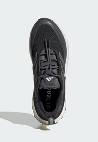 Baskets noires et grises avec un dessus en mesh, langue rembourrée et semelle blanche. Le design comprend trois bandes et le logo "ULTRABOOST".