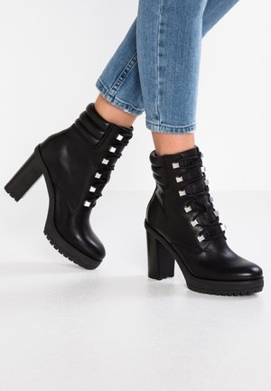 Bottines à talons noirs en cuir lisse avec un lacet, dotées d'accents argentés et d'une semelle texturée. Talon épais.