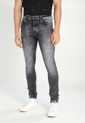 Slim-fit grijze jeans met een vervaagde wassing, vijf zakken en een knoopsluiting, gecombineerd met witte sneakers voor een casual look.