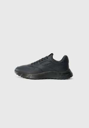Black athletic shoes with a smooth leather upper, rounded toe, cushioned sole, and contrasting textured accents along the sides.