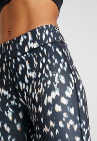 Leggings con un diseño ajustado, fabricados con una tela elástica que presenta un fondo oscuro con manchas abstractas en blanco, azul y naranja.