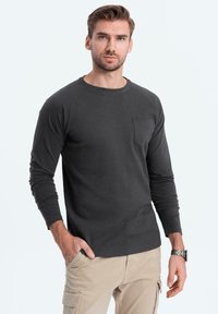 Tummanharmaa pitkähihainen paita, jossa on ribbauspinta ja pyöreä kaula-aukko, jossa on rintatasku. Yhdistetty vaaleanbeigeihin cargo-housuihin.