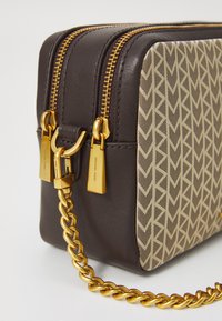 Brūna ādas crossbody soma ar ģeometrisku rakstu bēšā krāsā, zeltainu aprīkojumu, diviem rāvējslēdzējiem un zelta ķēdes siksnu.