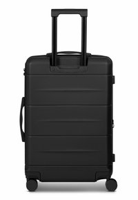 Valigia rigida nera con design segmentato, manico retrattile, maniglie superiore e laterale, e quattro ruote per la mobilità.
