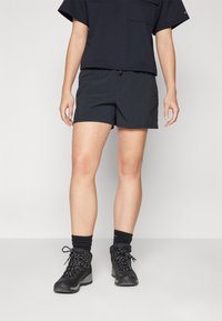 Pantalones cortos negros de tejido ligero con cintura elástica y cordón. Combinados con botas de senderismo negras y calcetines oscuros.