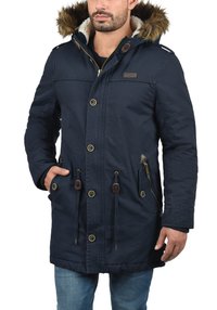 Marineblauwe parka met nepbontkraag, knoop- en ritssluitingen, zijzakken, taillekoord en textuurstof.