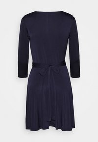 Robe bleu marine mi-longue jusqu'aux genoux avec manches trois-quarts et ceinture nouée à la taille, vue de dos sur un fond blanc.