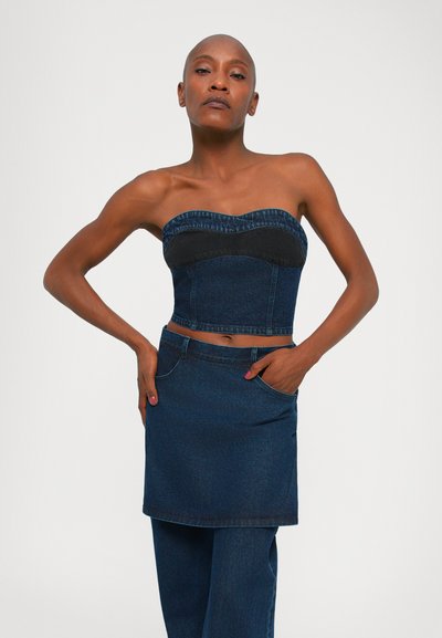 Denim crop-top dengan panel hitam yang terstruktur, dipadukan dengan rok denim lilit yang serasi dan celana jeans lurus, semuanya dalam warna gelap.