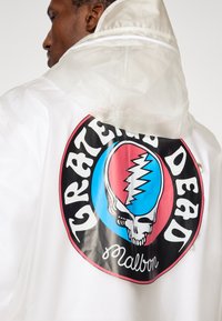 Διαφανές λευκό αδιάβροχο με μεγάλο κυκλικό σχέδιο στην πλάτη που απεικονίζει κρανίο, αστραπή και το κείμενο «Grateful Dead».