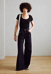 Černý přiléhavý top spárovaný s vysokými, širokými džínami z tmavého denimu. Doplněno bílou kabelkou přes rameno. Jednoduchý, moderní design.