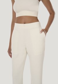 Kremfarvede, tætsiddende joggingbukser med sidelommer, lavet af blødt stof med en glat tekstur og en tilspidset benform.