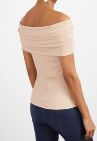 Top bez ramínek, žebrovaný v jemné béžové barvě s drapérií na výstřihu. Stylizováno s námořnickými legínami, které ukazují fitted siluetu.